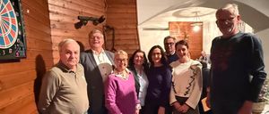 Eine Gruppe von Menschen in formeller Kleidung, lächelnd, stehen zusammen in einer Innenumgebung mit Holzwänden und Deckenlampen.