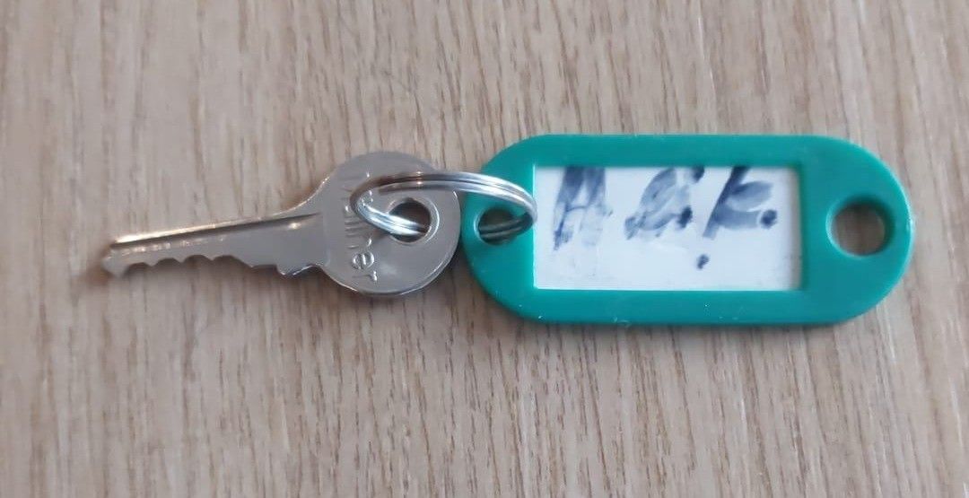 A key with a teal plastic label displaying blue text reading 'A.E.F.' is on a wooden surface.