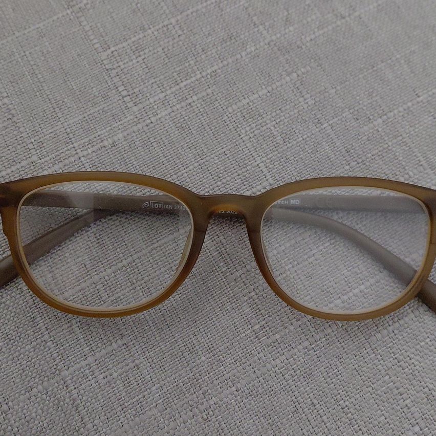 A pair of brown-framed glasses with clear lenses rests on a textured gray surface. The frame is made of a material that resembles wood.