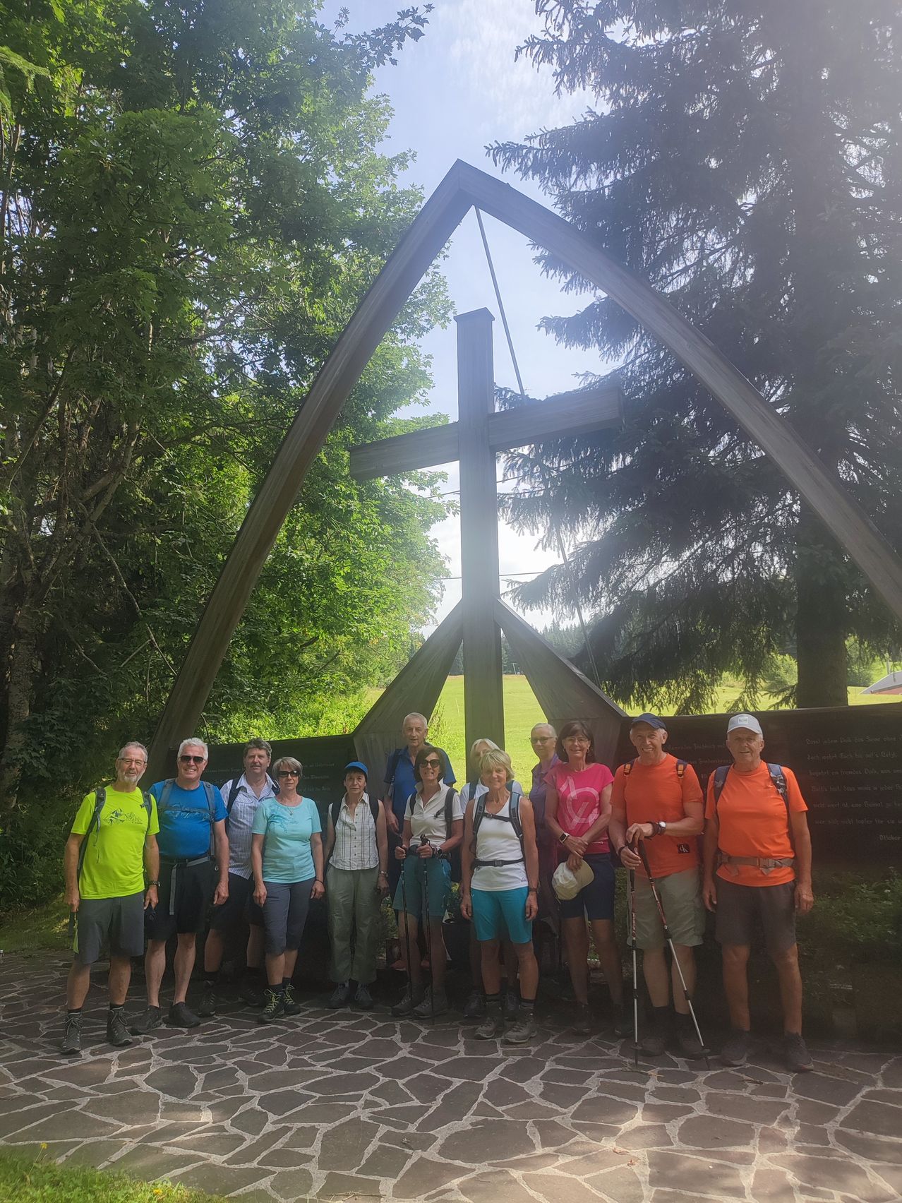 A group of hikers pose for a photo in front of a wooden cross in a forest.