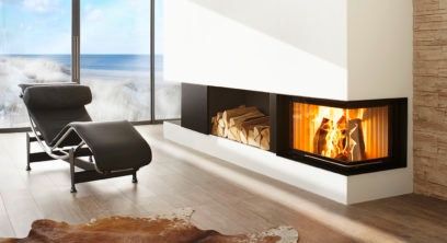 A modern living room with a fireplace, a lounge chair, a rug, and a large glass window overlooking the ocean.