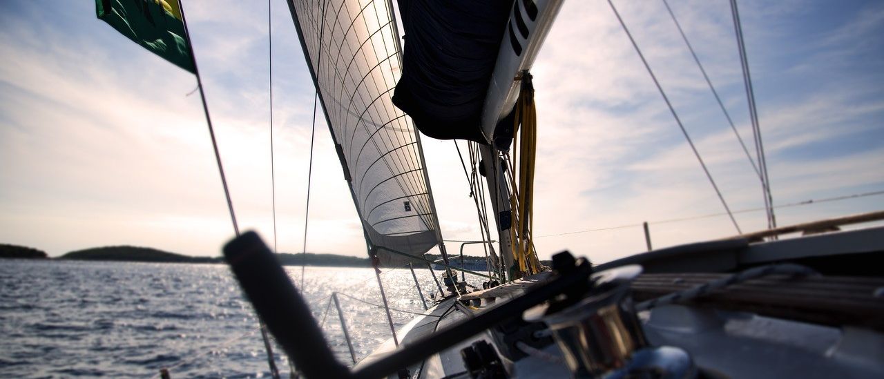 Ein Segelboot mit einer farbenfrohen Flagge segelt auf einem ruhigen Ozean, mit der Sonnenreflexion, die auf dem Wasser schimmert.