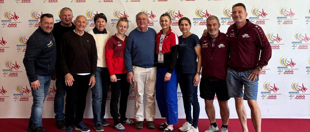 Eine Gruppe von Menschen, die vor einer Wand mit verschiedenen Logos, darunter dem Logo der European Judo Championships, für ein Foto posieren.