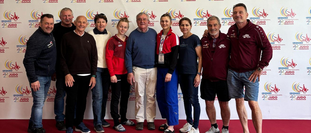 Eine Gruppe von Menschen, die vor einer Wand mit verschiedenen Logos, darunter dem Logo der European Judo Championships, für ein Foto posieren.