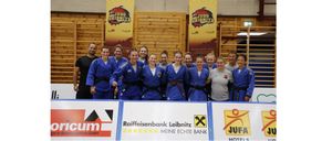Eine Gruppe von Judoka steht in einer Turnhalle mit zwei Bannern hinter ihnen. Sie tragen blaue Uniformen. Ein Banner sagt 'JUDOLEIBNITZ' und das andere hat einen roten Drachen.