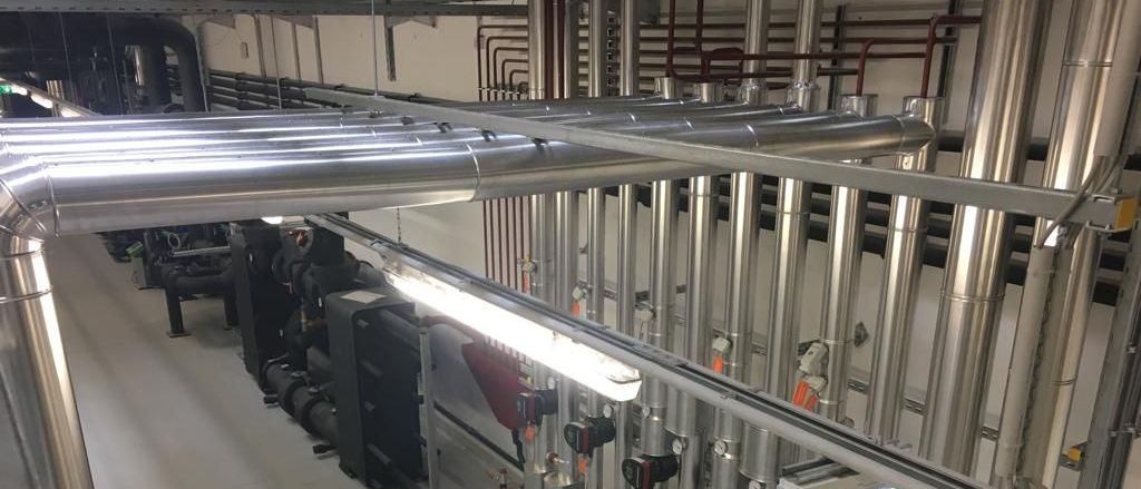 Ein Industriebetrieb mit mehreren Edelstahlrohren und Maschinen. Ein grünes Notfallschild ist sichtbar, und eine Leuchtstofflampe beleuchtet den Bereich.