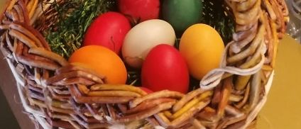 Ein Korb mit Ostereiern auf einer Theke, dekoriert mit Blumen und Zweigen. Ein Blumenvase und ein Salzstreuer sind ebenfalls auf dem Tisch.