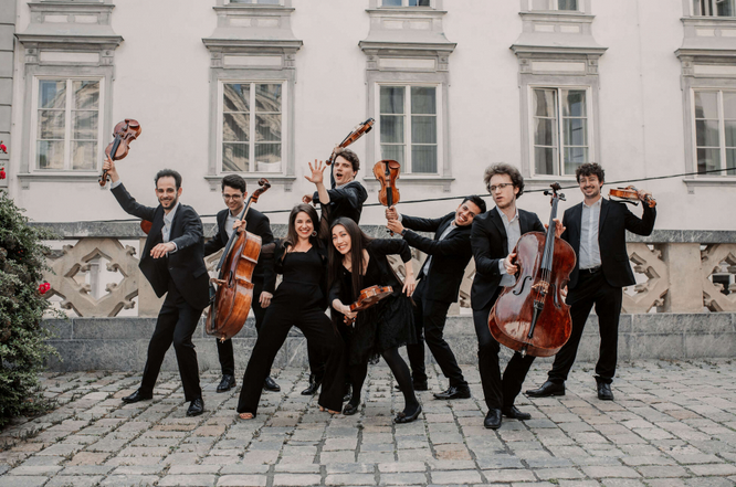 Eine Gruppe von Musikern posiert mit ihren Instrumenten vor einem Gebäude für ein Foto.