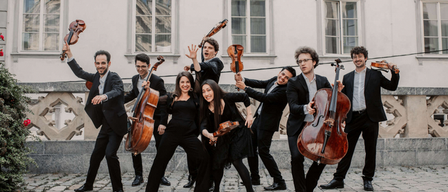 Eine Gruppe von Musikern posiert mit ihren Instrumenten vor einem Gebäude für ein Foto.