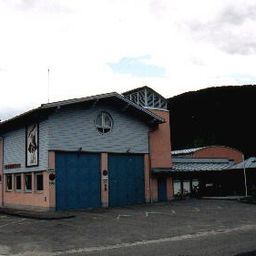Ein Gebäude mit einer blauen Tür und einem runden Fenster in der Mitte, vor einem großen Berg gelegen. Das Gebäude scheint eine Feuerwache zu sein, mit einem Schild an der Wand.