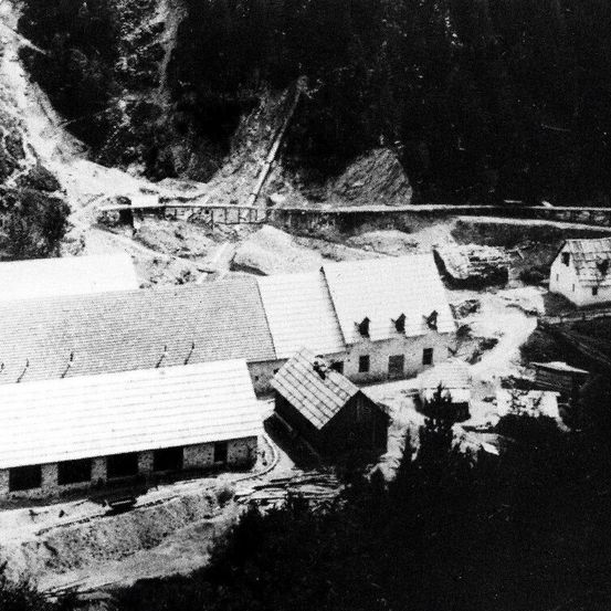 Eine Draufsicht auf eine Baustelle mit mehreren Gebäuden und Strukturen im Bau, umgeben von Bäumen und Hügeln.