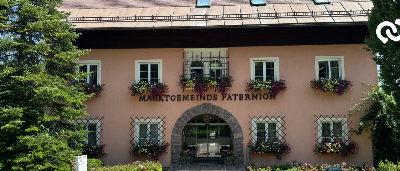 A pink building with arched entrance and 'Marktgemeinde Paternion' written above it. It has multiple windows with white frames and flower boxes.