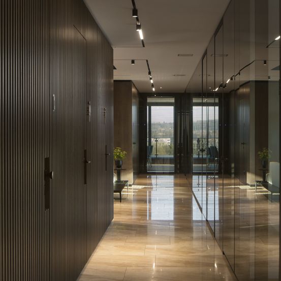 Ein leerer Flur mit Holzböden und Glaswänden, mit einem Topf mit Pflanzen und einem Tisch mit einer Glastür, die zu einem Balkon führt.