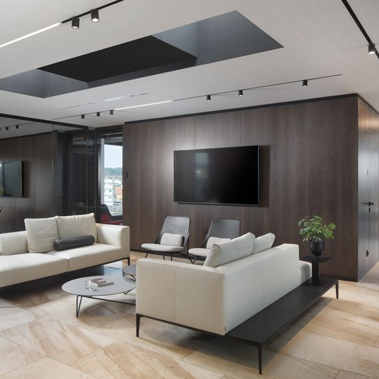 Ein modernes Wohnzimmer mit Holzwänden, zwei weißen Sofas, einem runden Tisch und einem Flachbildfernseher an der Wand.