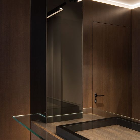 Ein modernes Interieur mit Holzwänden, einer Glastür und einem Glasregal, beleuchtet von einer Deckenleuchte.