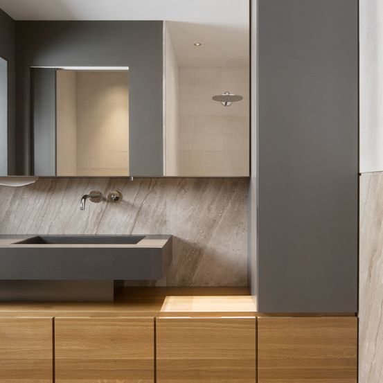 Ein modernes Badezimmer mit einer grauen Marmorwand, einem Holzschrank, einem Waschbecken, einem Wasserhahn und einer Dusche darüber.