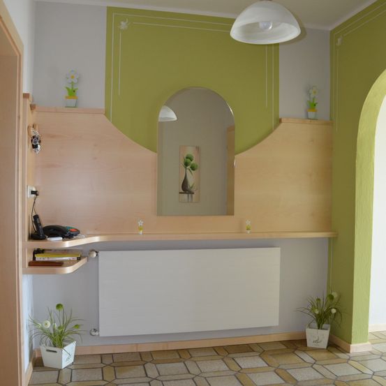 Ein leerer Raum mit einem weißen Heizkörper, grünen Wänden und Holzregalen mit Pflanzen und einem Telefon.