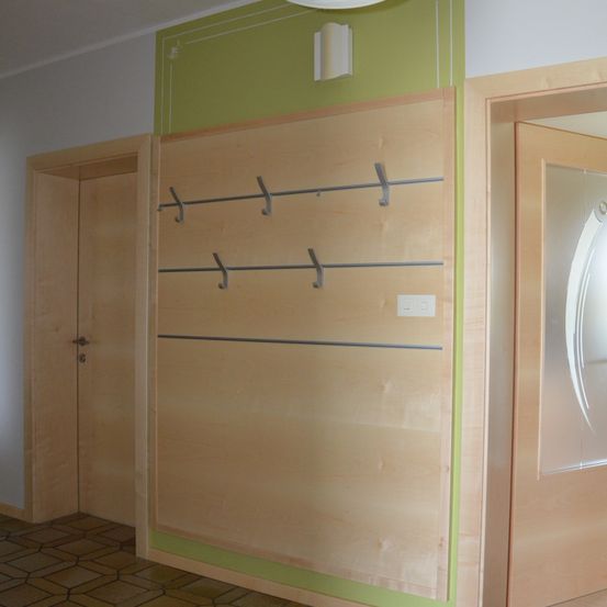 Eine Holzwand mit Kleiderhaken und einer Deckenleuchte. Auf beiden Seiten der Wand befinden sich zwei Türen. Der Boden ist gefliest.
