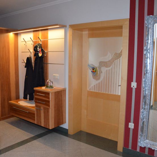 Ein Flur mit Holzschrank, einer Bank und einer Glastür mit einem farbenfrohen Design. Die Wände sind rot und weiß gestreift.