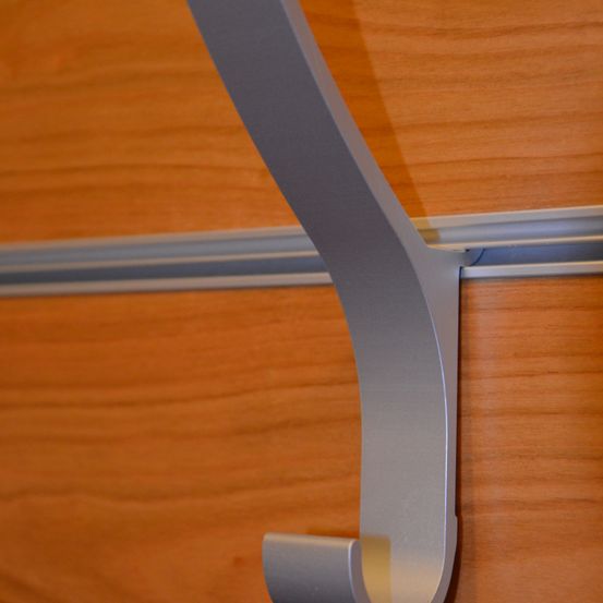 Eine Nahaufnahme eines silbernen Metallhakens, der an einer hölzernen Wand mit einem Metallstreifen oben montiert ist.