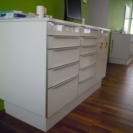 Ein weißer Schrank mit mehreren Schubladen und einem Monitor oben, an einer grünen Wand, mit Holzböden.