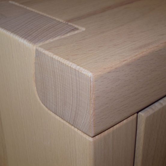 Ein Nahaufnahme einer hölzernen Schrankecke mit einer polierten Oberfläche. Die Maserung des Holzes ist sichtbar und zeigt natürliche Linien und Texturen.