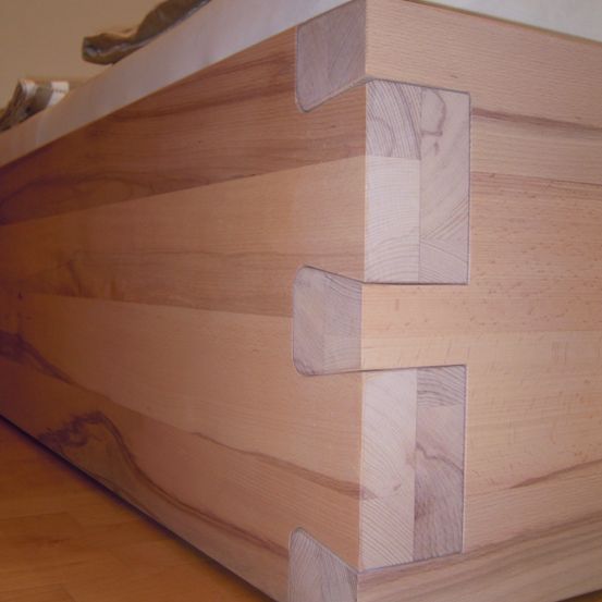 Ein Nahaufnahme von Holzplanken mit sichtbaren Verbindungen, die eine komplizierte Zimmermannsarbeit an einer Holzstruktur zeigt. Die Maserung des Holzes ist sichtbar und die Verbindungen sind eng aneinandergefügt.