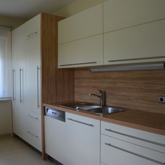 Eine moderne Küche mit Holzarbeitsplatte, Edelstahlspüle, Wasserhahn, Geschirrspüler und weißen Schränken mit Holzakzenten.