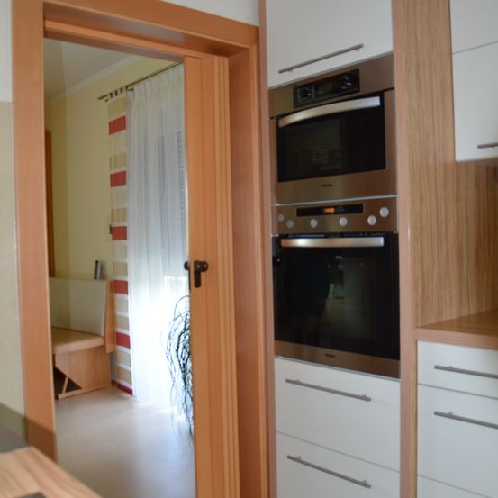 Eine moderne Küche mit Holzschränken und Edelstahlgeräten, einschließlich eines Doppelofens und eines Fensters mit weißen Vorhängen.