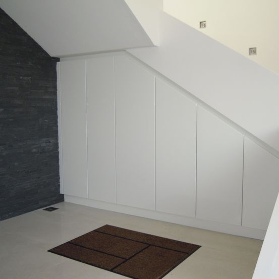 Ein leerer Raum mit weißen Wänden, einer schwarzen gefliesten Wand und einem braunen Teppich auf dem Boden. Weiße Schränke sind an der Wand befestigt.