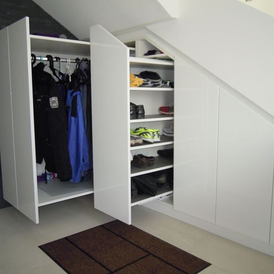 Ein weißer Kleiderschrank mit Schiebetüren ist geöffnet und zeigt Kleidung an Kleiderbügeln und Schuhe auf Regalen. Der Kleiderschrank steht in einer Ecke des Raumes.