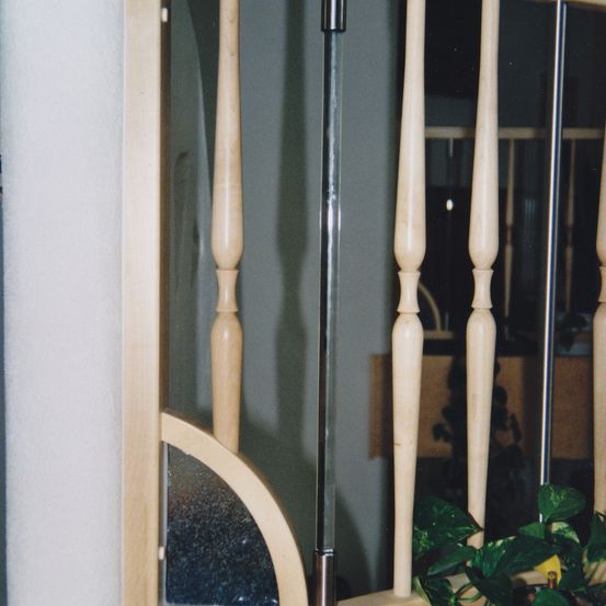 Eine Nahaufnahme eines hölzernen Handlaufs an einer Treppe mit einer klaren Glasscheibe und einer Pflanze.