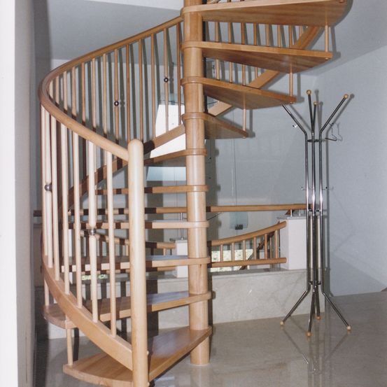 Eine moderne Holzwendeltreppe mit Marmorboden. Sie zeichnet sich durch ein schlankes Design aus und befindet sich neben einem Kleiderständer.