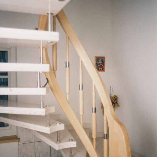 Ein Nahaufnahme einer Holztreppe mit einem weißen Marmorgeländer, modernen Metallakzenten und einem dekorativen Bilderrahmen an der Wand.