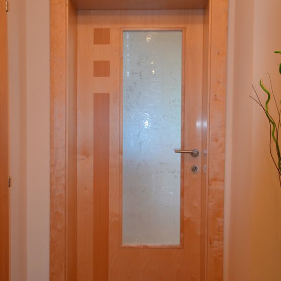 Eine Holztür mit mattierten Glasscheiben und einem silbernen Griff, mit einem einfachen geometrischen Muster auf der Türtafel.