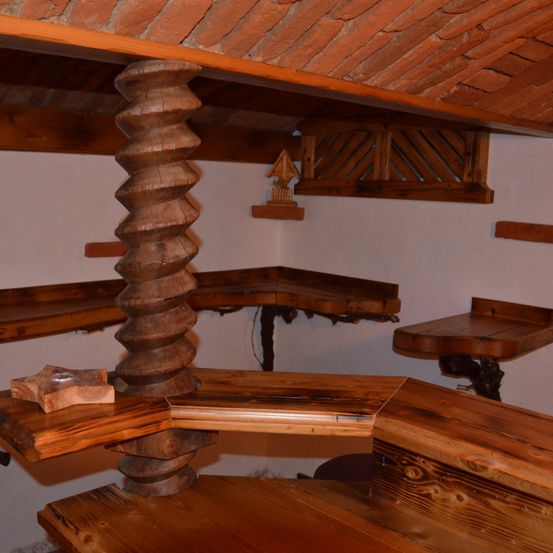 Ein Innenbereich mit Ziegeldecke und hölzerner Spiralsäule. Es gibt Holzregale an den Wänden. Ein kleines Holzobjekt befindet sich auf dem linken Regal.