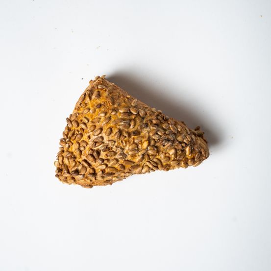 Ein dreieckiges Stück Brot mit Samen auf einer weißen Oberfläche, wahrscheinlich Sesamsamen.