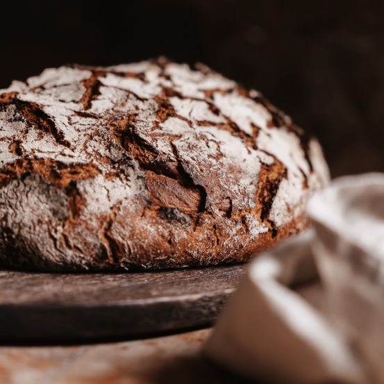 Eine Nahaufnahme eines rustikalen, vollwertigen Laibs Brot mit dicker Kruste, der auf einem Holzbrett liegt.