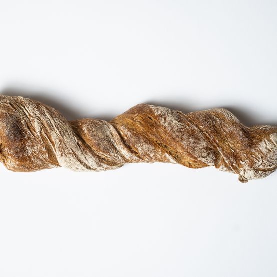 Ein langes, verdrehtes Brot mit einer goldbraunen Kruste liegt auf einer weißen Oberfläche.