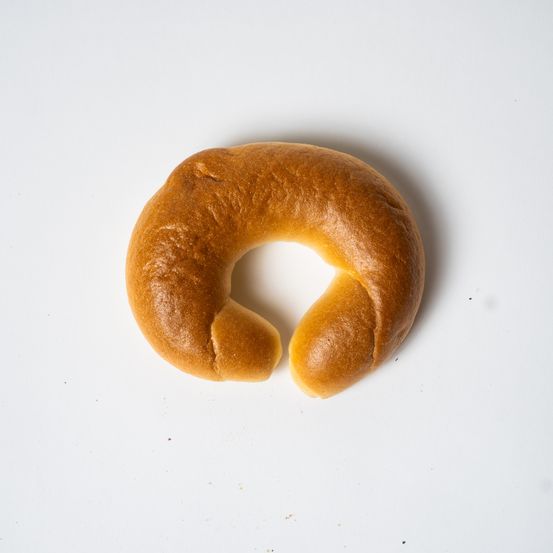 Ein goldenbrauner Brezel liegt auf einer weißen Oberfläche. Der Brezel ist leicht geöffnet und zeigt seine innere Struktur.