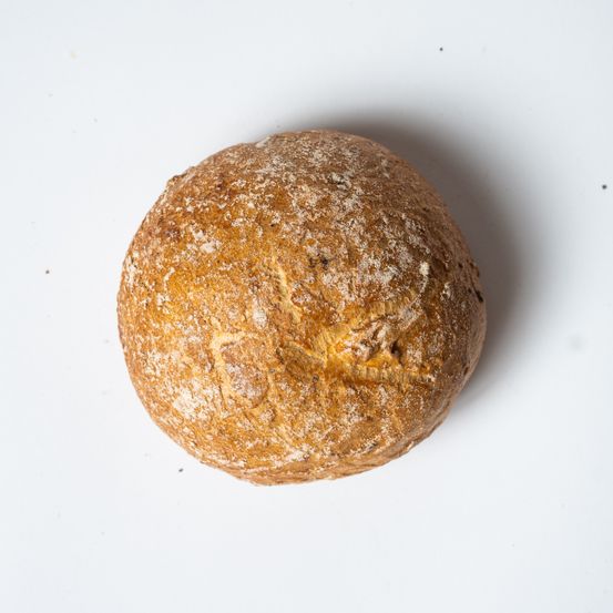 Ein runder Laib Brot mit goldenbrauner Kruste und weißer Mehlbestäubung wird auf einer weißen Oberfläche gezeigt.