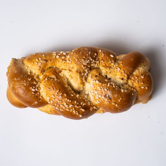 Eine Nahaufnahme eines gebackenen, gebratenen Brotlaibes mit einer goldbraunen Kruste und gestreuten Sesamkörnern auf einem weißen Hintergrund.