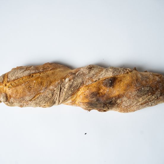 Ein Laib rustikales Brot wird auf einem weißen Hintergrund gezeigt. Das Brot hat eine goldbraune Kruste und eine leicht verdrehte Form.