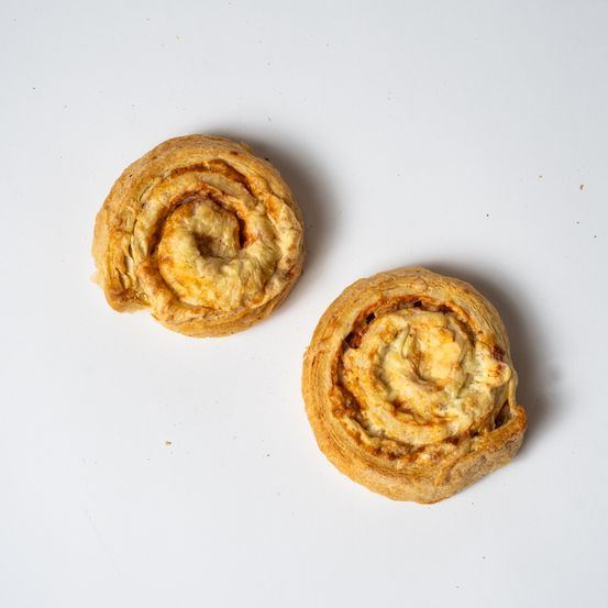 Zwei spiralförmige Gebäckstücke liegen auf einer weißen Oberfläche. Jedes Gebäck hat eine goldbraune Kruste und eine Füllung, die wie Käse aussieht. Die Gebäckstücke sind leicht unterschiedlich in Größe und Form.