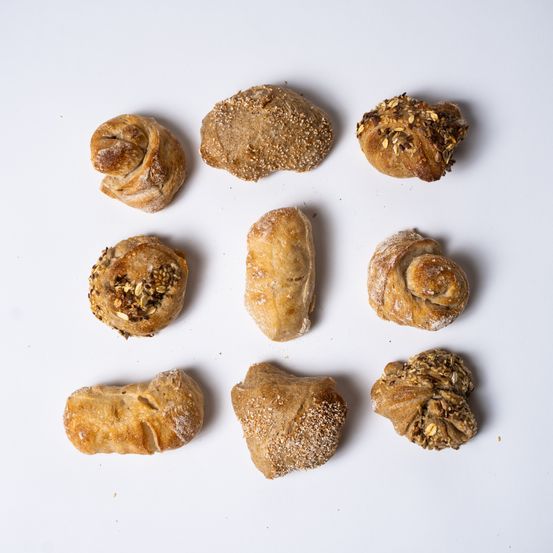 Eine Sammlung verschiedener Gebäckstücke auf einer weißen Oberfläche, darunter Brötchen, Brot und Croissants mit Toppings.