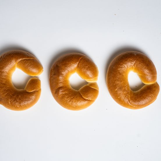 Drei goldbraune Brezeln sind in einer Reihe auf einem weißen Hintergrund angeordnet. Jede Brezel ist verdreht und geformt, um eine Öffnung in der Mitte zu schaffen. Die Oberfläche der Brezeln zeigt eine leicht strukturierte Kruste.