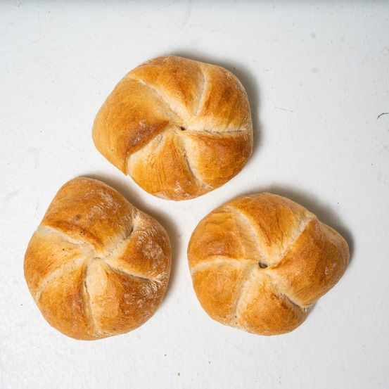 Drei runde, goldbraune Gebäckstücke mit aufwendigen Kreuzmustern auf der Oberseite, auf einer weißen Oberfläche angeordnet.