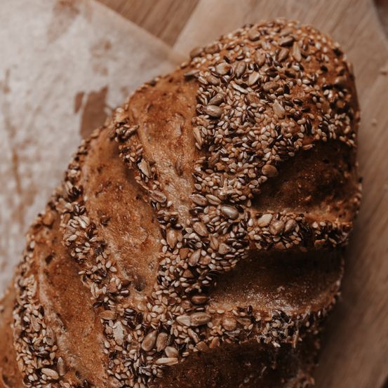 Ein Laib Brot mit Sesamkörnern auf einem Holzbrett. Das Brot ist in zwei Hälften geschnitten.