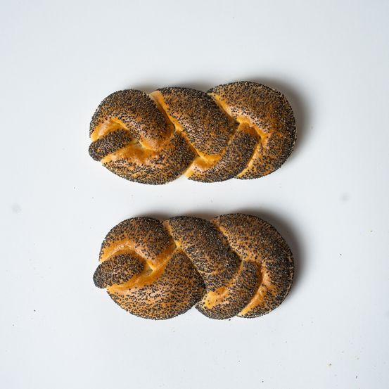 Zwei geflochtene Gebäckstücke mit goldener Kruste und schwarzen Samen sind auf einer weißen Oberfläche zu sehen.