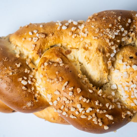 Eine Nahaufnahme eines geflochtenen Brotlaibs mit grobem Salz darüber gestreut, auf einem weißen Hintergrund präsentiert.